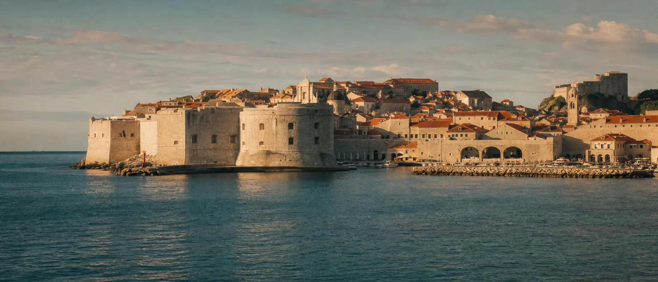Dubrovniks Altstadt mit Festungsmauern und roten Dächern im morgendlichen Licht, vom Meer aus gesehen.