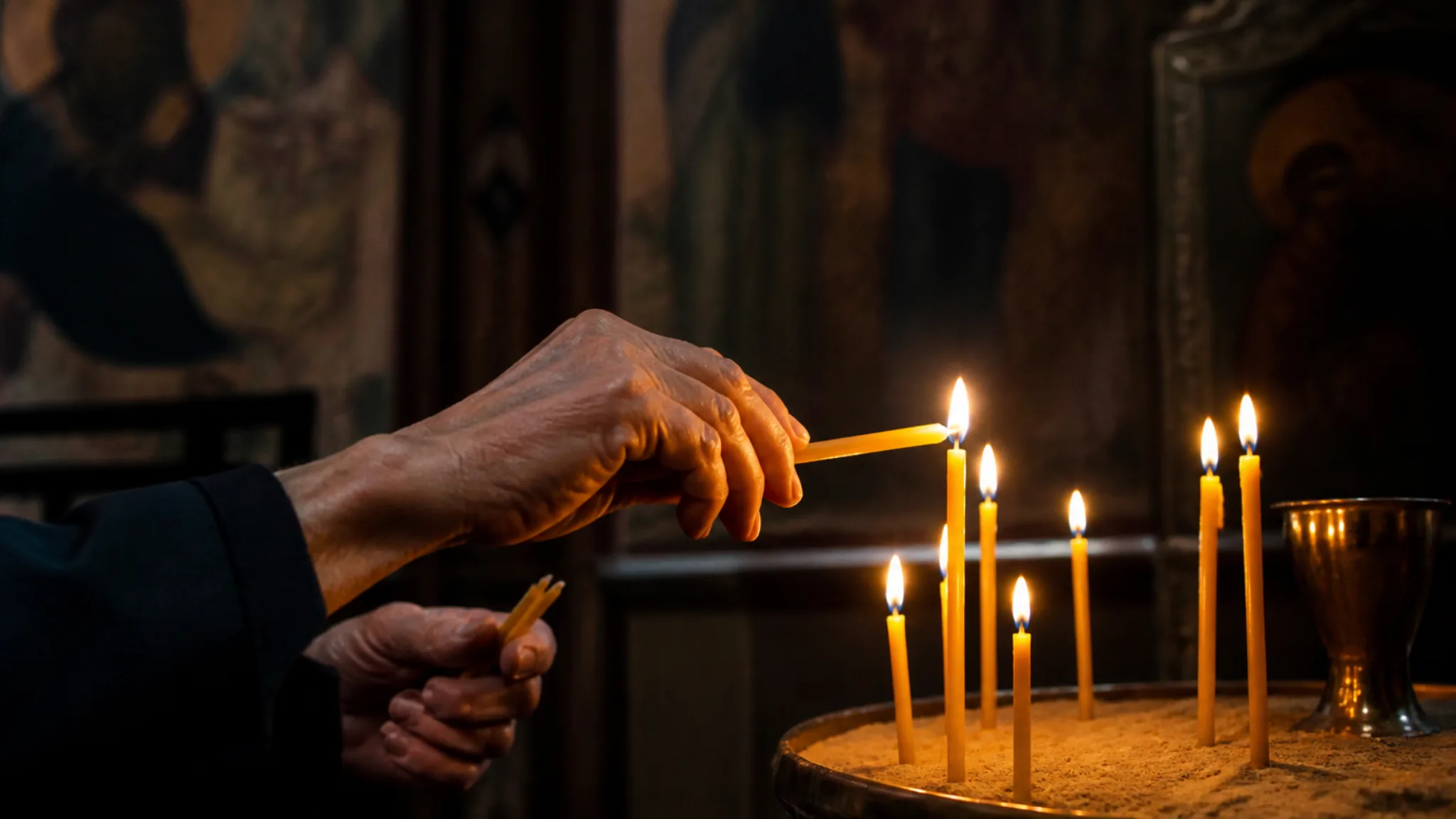 Hände eines älteren Menschen entzünden eine Kerze in einer orthodoxen Klosterkirche.