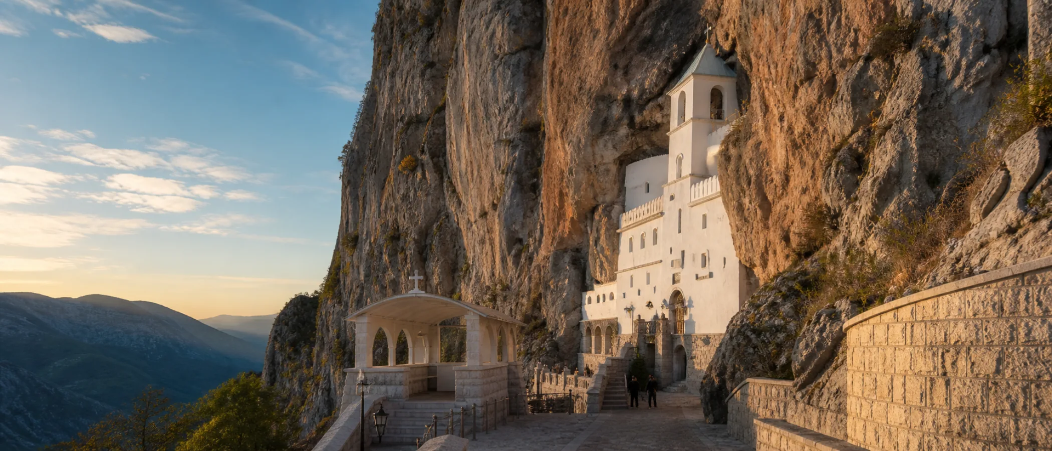 Das weiß leuchtende Kloster Ostrog in einer steilen Felswand im morgendlichen Licht.